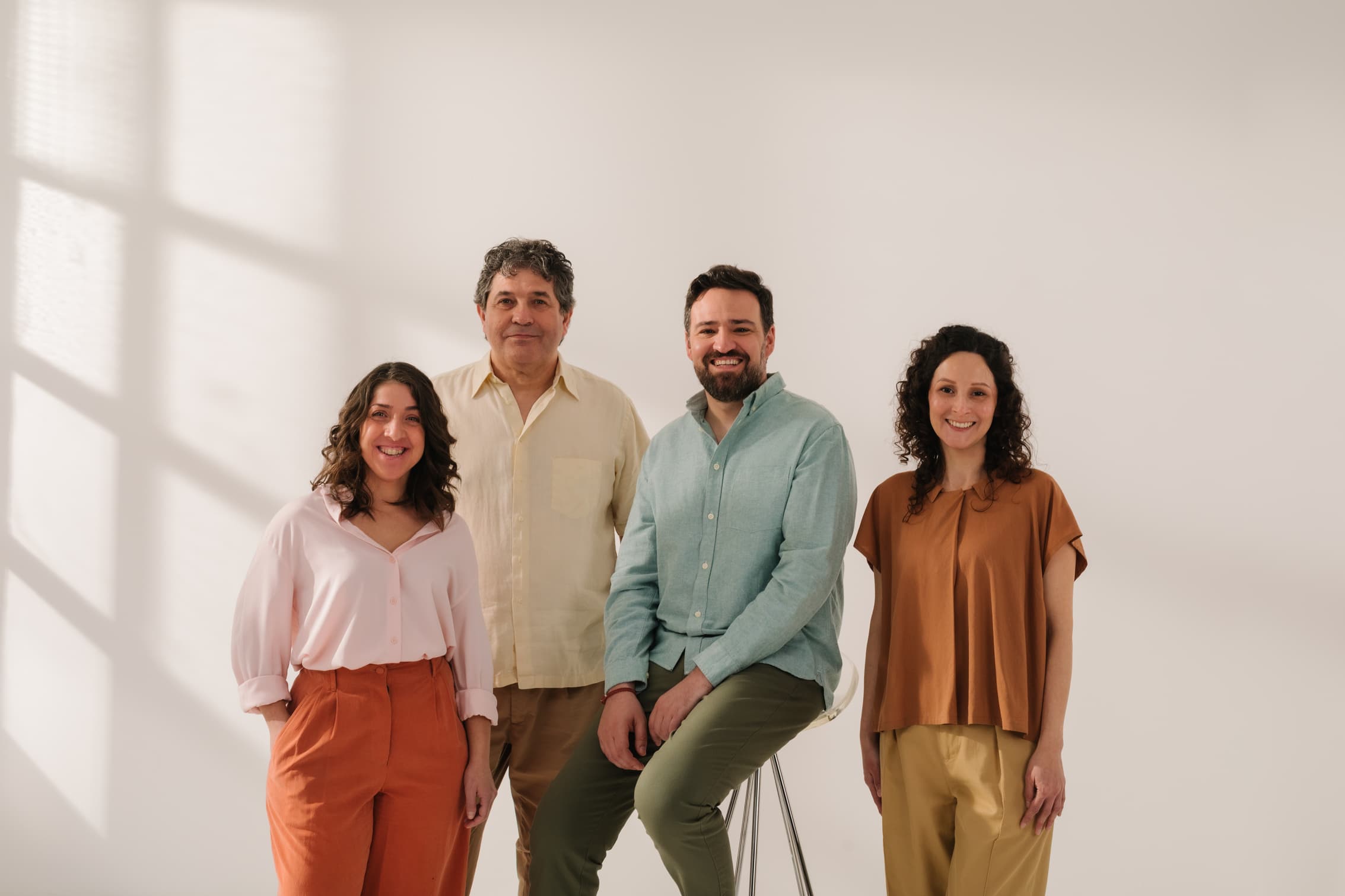 Four professionals in casual business attire stand together against a plain white wall, smiling for a group portrait.