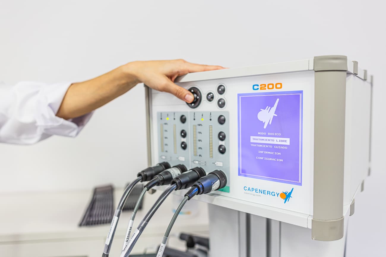 Clinician operating a Capenergy C200 radiofrequency device with connected cables and interface screen.