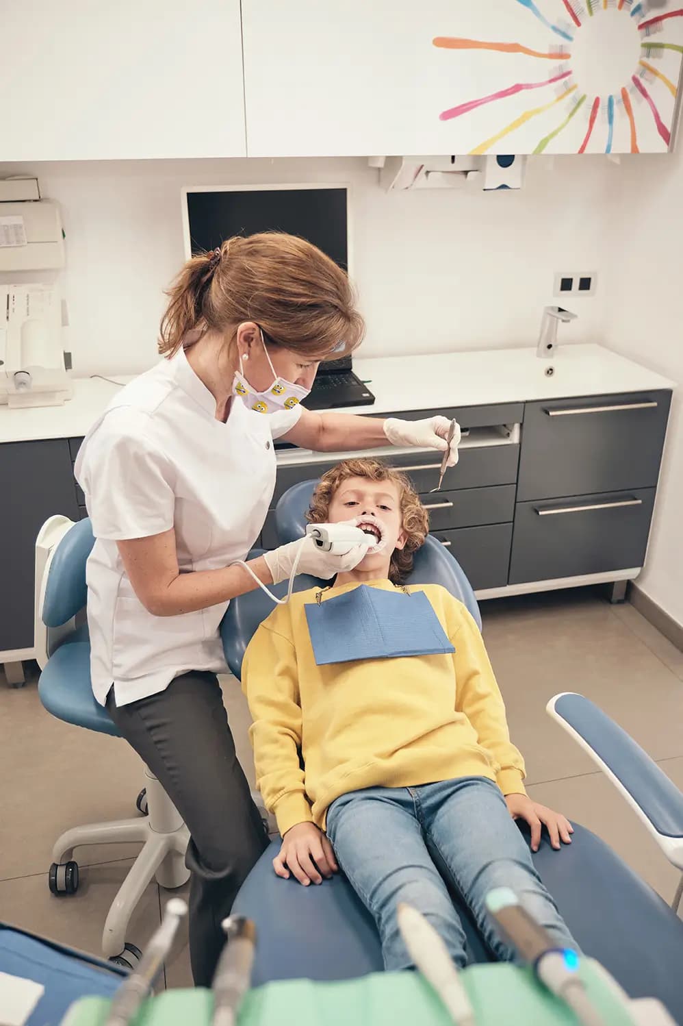 Dental professional using a handheld intraoral scanner on a young patient in a modern clinical setting.