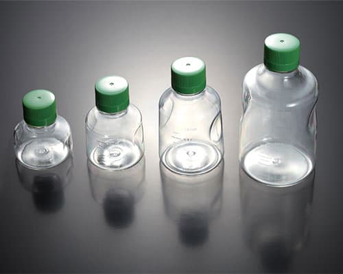 Four clear polycarbonate laboratory bottles of varying sizes, each featuring a green screw cap, arranged in a row on a dark surface.