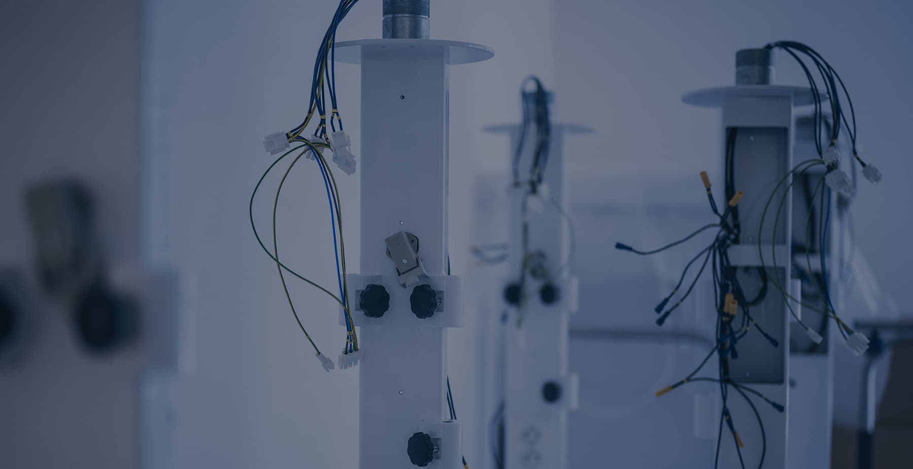 Multiple white vertical medical equipment support columns with exposed wiring and internal components standing in a clean manufacturing or assembly environment.