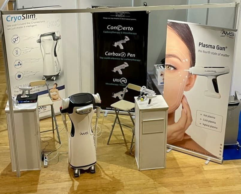 A trade show display featuring multiple AAMS medical devices, including various aesthetic treatment systems and branded signage.