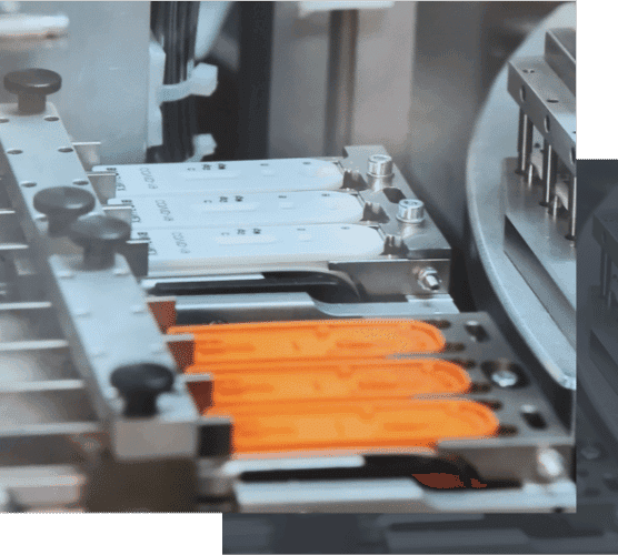 Automated production line machinery processing white and orange diagnostic test cassettes within a clean manufacturing facility environment.