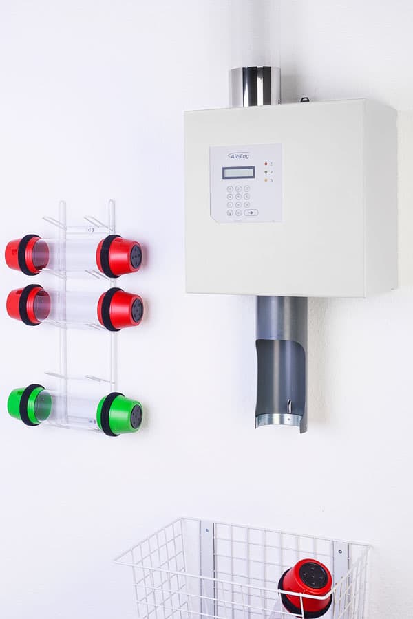 Pneumatic tube station unit displayed with multiple transport carriers in a wall-mounted storage rack.