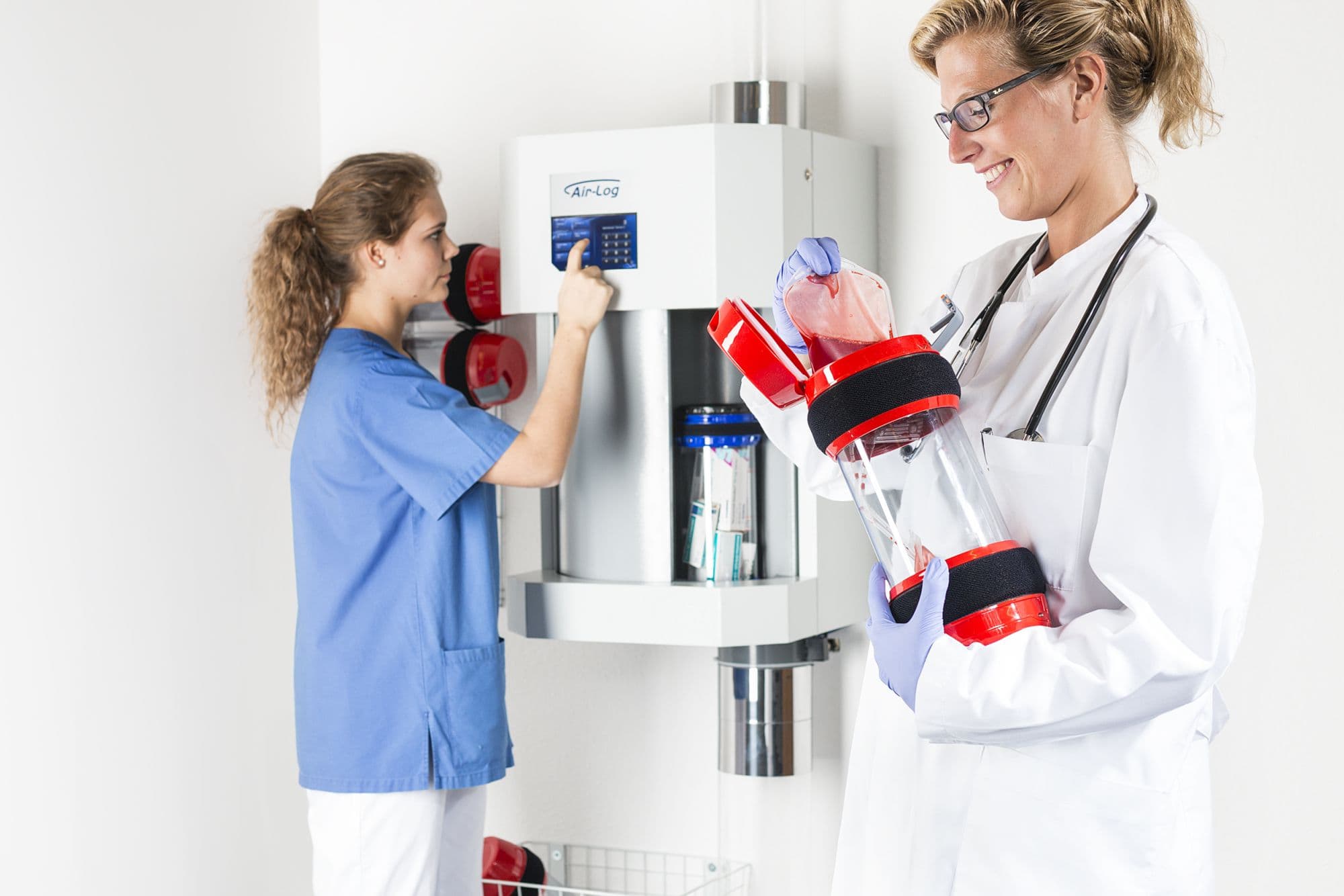 Medical staff operating a pneumatic tube station to transport blood samples in a hospital setting.