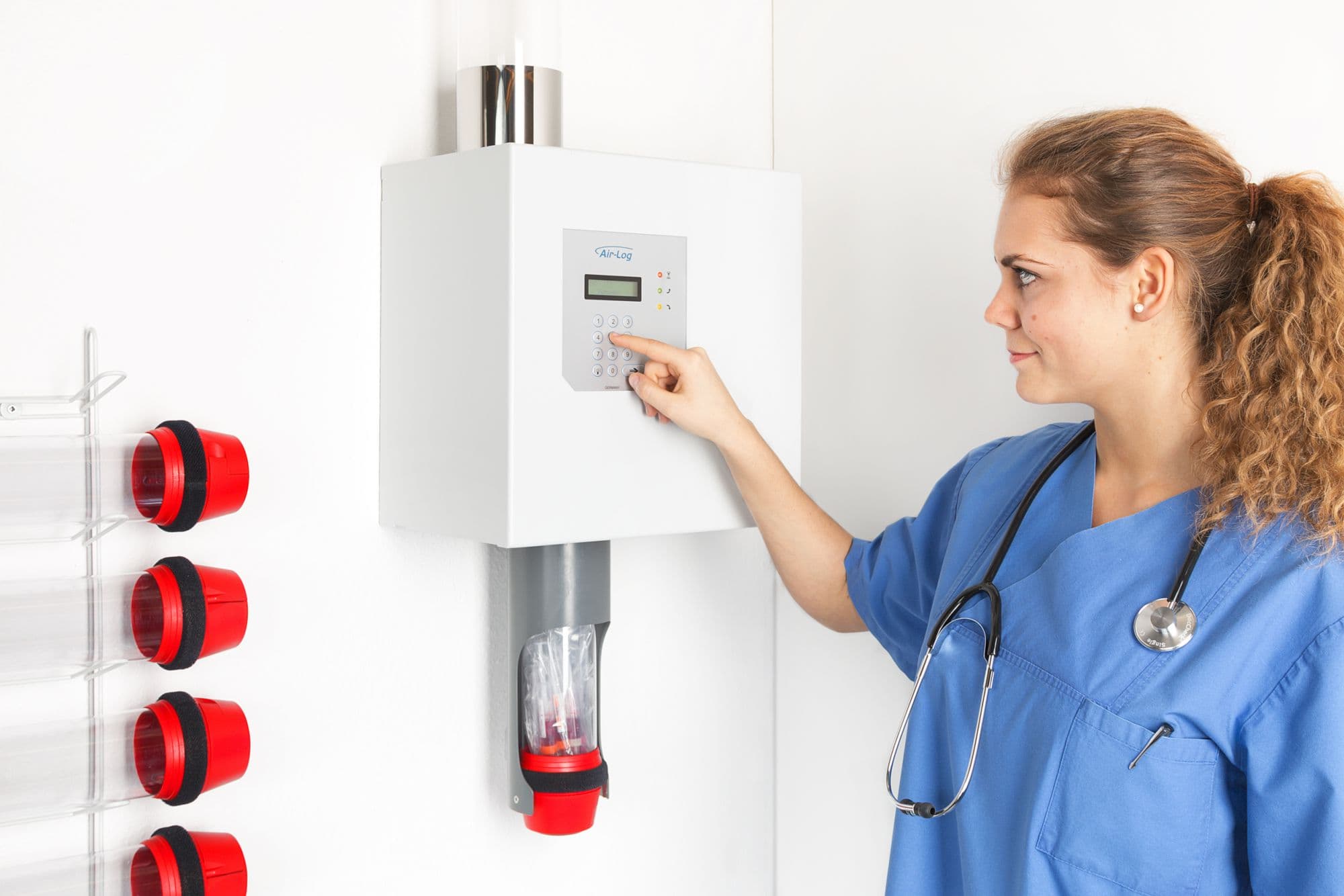 Nurse using a wall-mounted pneumatic tube station to send a sample carrier in a hospital.