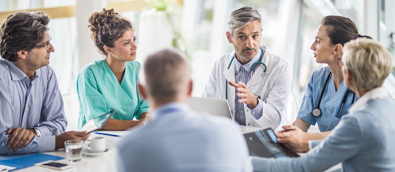 Medical team and professionals in a collaborative meeting, reviewing documents and discussing clinical strategies.