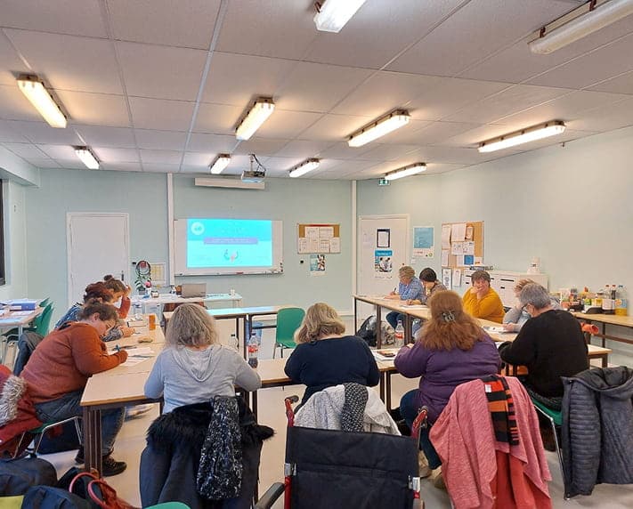 A group of people seated at tables in a classroom setting, attending a professional training session with a projector screen in front.