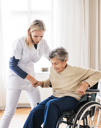 A healthcare worker in a white uniform assists an elderly woman in a wheelchair, appearing to be a generic stock medical photograph.