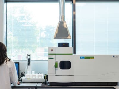 Laboratory technician operating advanced analytical instrumentation in a modern, well-lit pharmaceutical research facility.