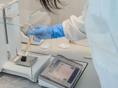 Close-up of a researcher using a precision analytical balance to weigh pharmaceutical samples in a laboratory.
