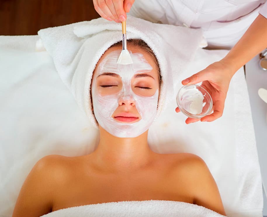 Professional aesthetician applying a facial mask treatment to a client in a clinical spa setting.