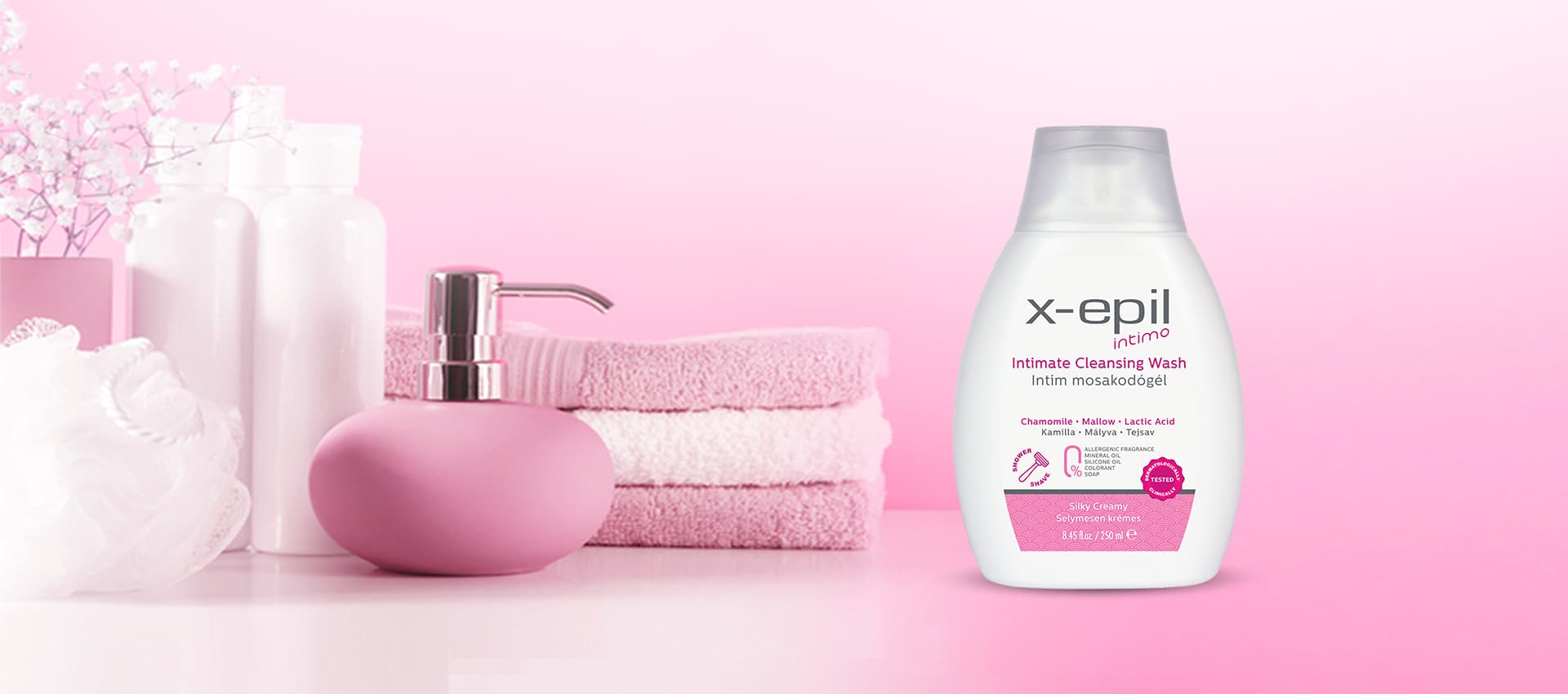 A single bottle of X-Epil intimate cleansing wash displayed next to pink towels and bathroom accessories on a soft pink background.