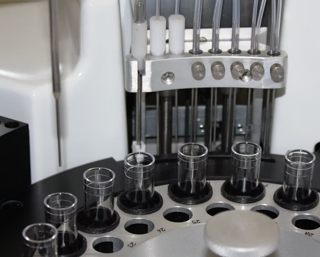 Close-up view of a laboratory diagnostic machine showing a circular sample tray with empty glass test tubes and metal dispensing needles.