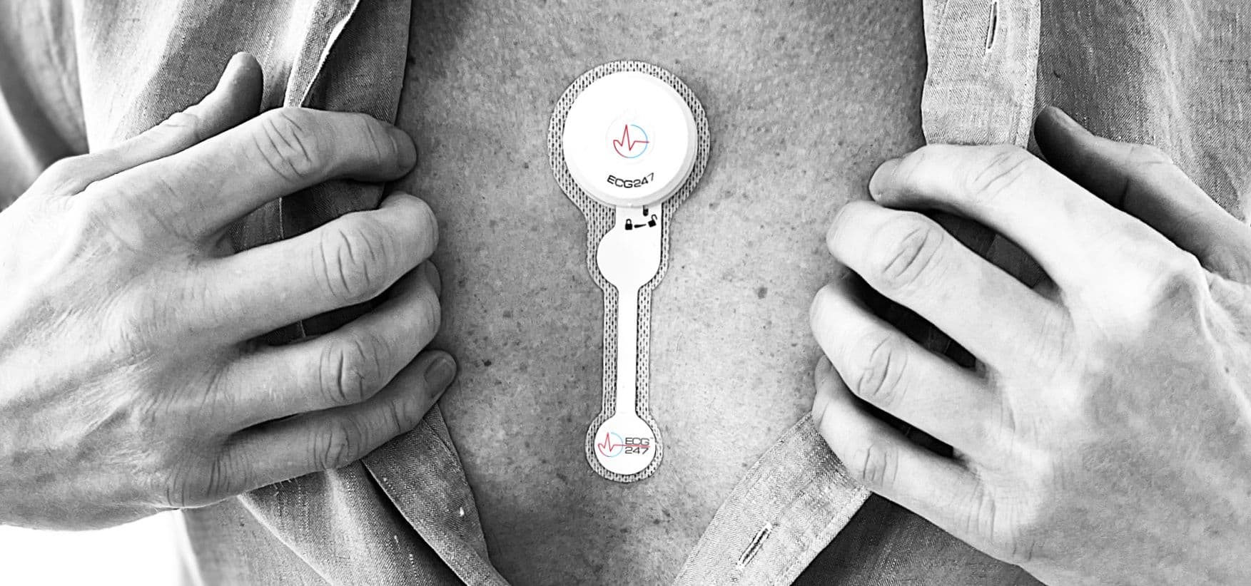 A man opens his shirt to reveal a single ECG247 heart monitoring sensor patch adhered to his chest skin.