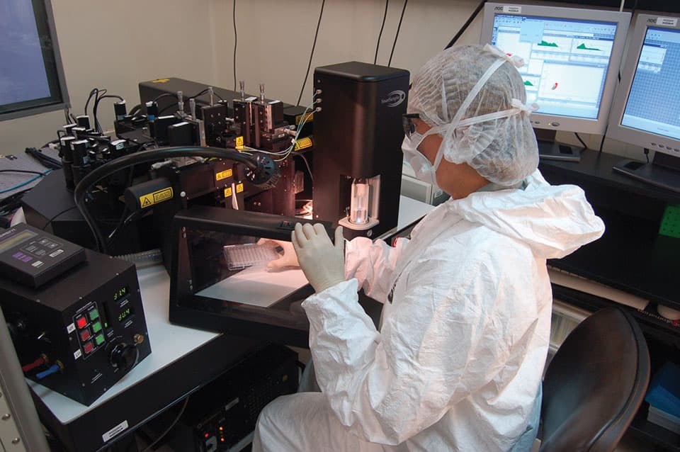 Technician in protective gear operating specialized laboratory equipment for biotechnological research and production processes.