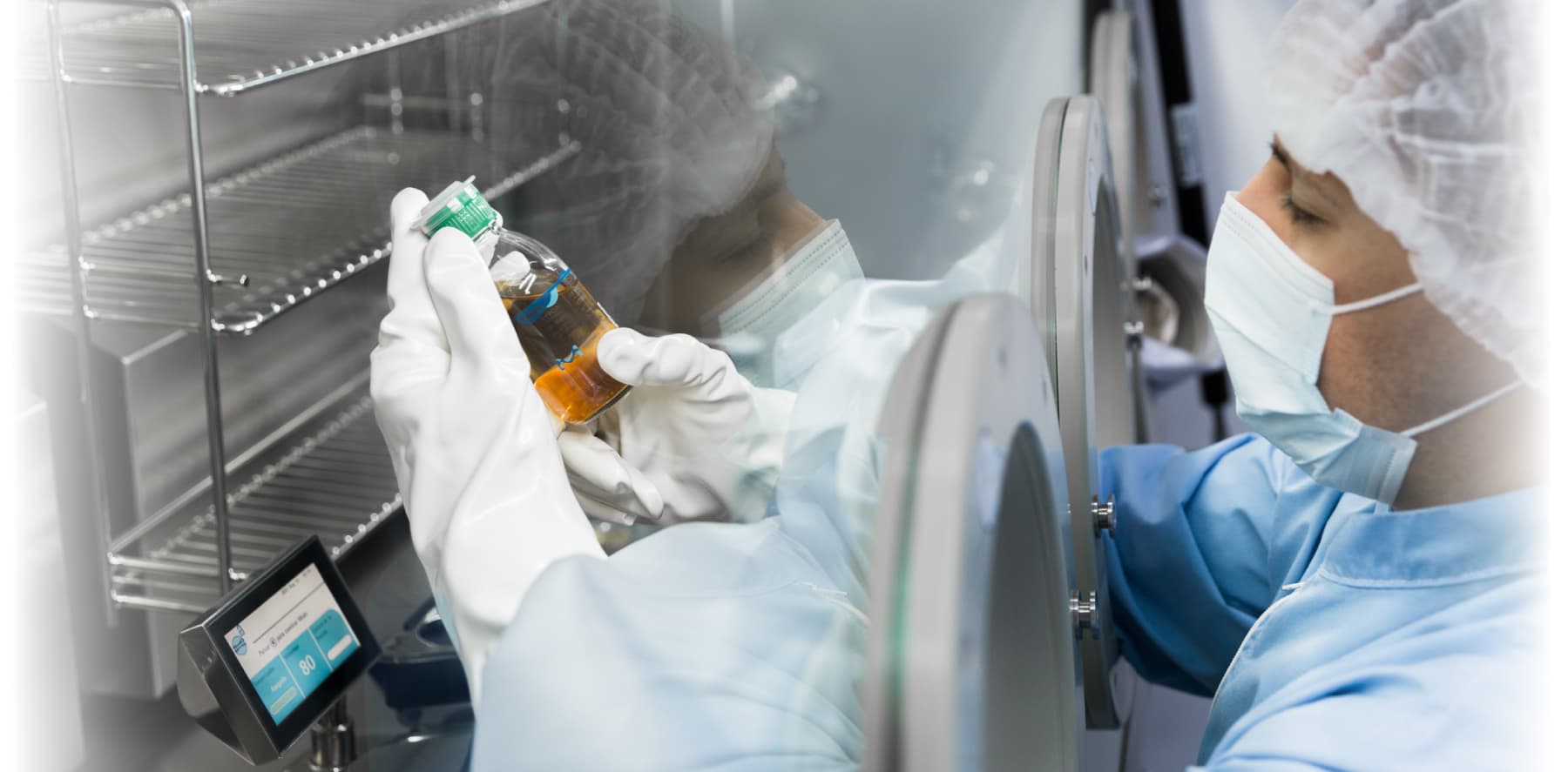 Researcher in a sterile environment handling a glass vial inside a controlled laboratory containment unit.