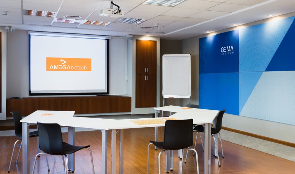 Modern corporate meeting room featuring a projector screen with company branding and modular seating arrangements.