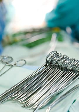 A close-up view of stainless steel surgical instruments arranged on a sterile blue cloth, with blurred medical staff in the background.