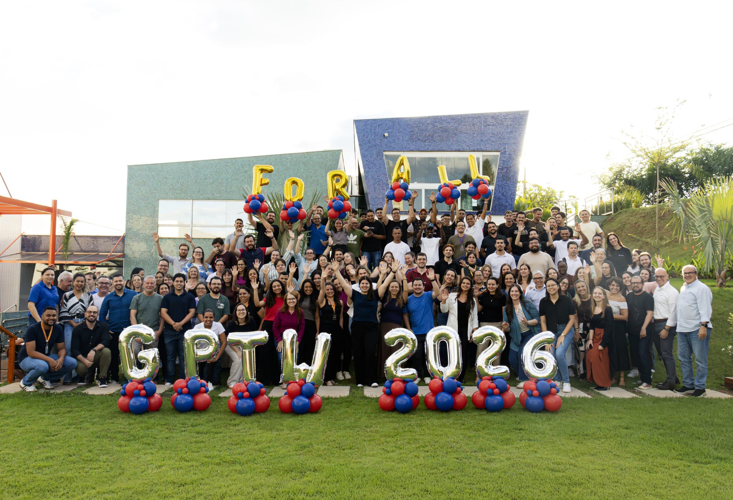 A large group of employees posing for a company photo in front of a building with balloons spelling GPTW 2026.