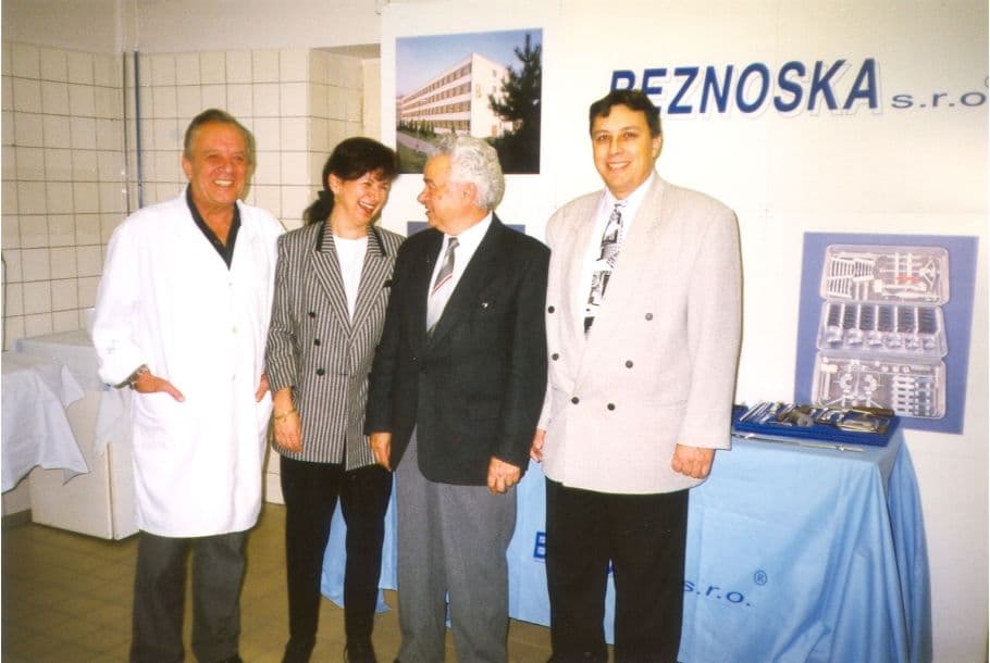 Four professionals stand together in front of a branded display booth featuring company signage and a medical instrument kit.