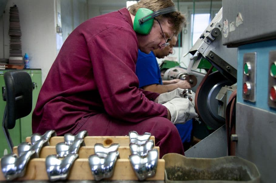 A technician in a workshop uses a grinding machine to process metallic knee joint components, with finished parts arranged in wooden racks.