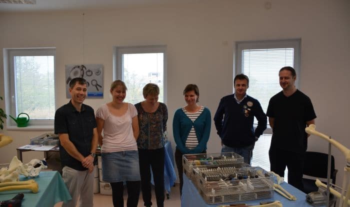 Six staff members stand together in a bright office space featuring tables with orthopedic surgical instruments and anatomical bone models.