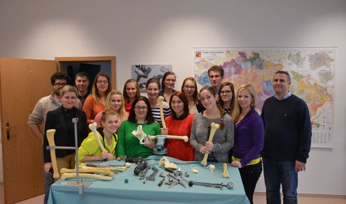 A group of employees standing behind a table covered with orthopedic surgical instruments and anatomical bone models in an office setting.