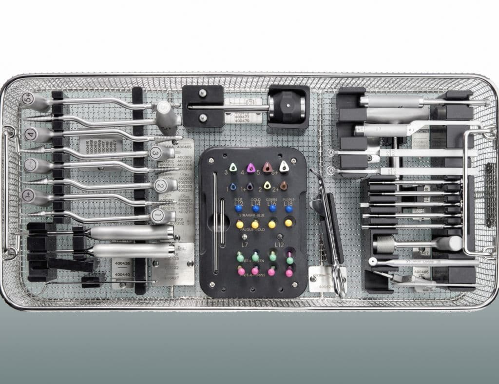 A surgical instrument sterilization tray containing a comprehensive kit of orthopedic tools, metal rods, and color-coded drill bits organized in slots.
