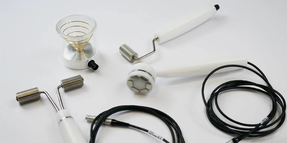 A collection of medical accessories including various metal roller applicators, a conical gold-wire device, and black connection cables on white background.