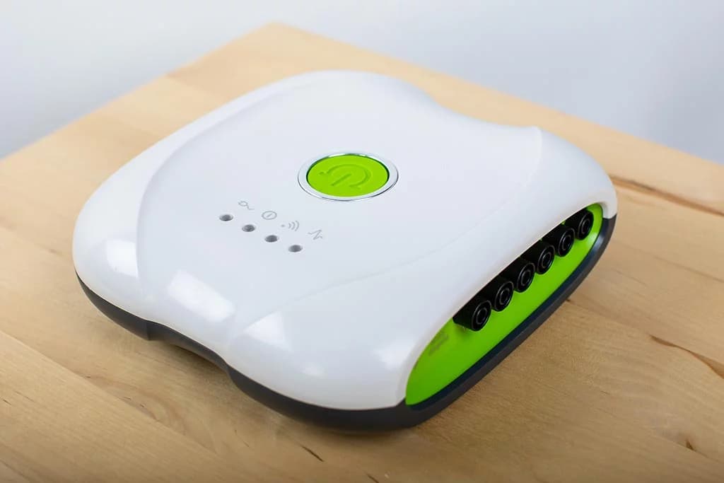 A single white and green medical device with a central power button and multiple side ports resting on a wooden surface.