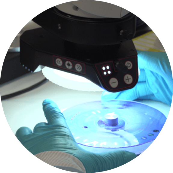 Laboratory technician using specialized microfluidic equipment to analyze diagnostic test discs in a controlled research environment.