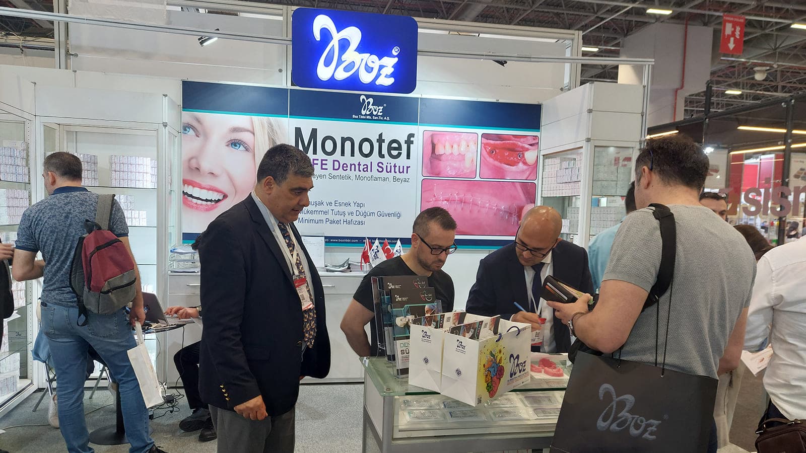 Company representatives interact with visitors at a branded trade show booth featuring dental suture product displays and promotional signage.