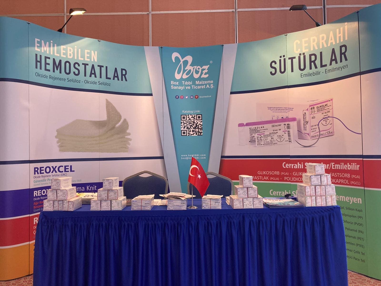 A trade show booth display featuring a blue draped table with stacked medical product boxes and branded signage for Boz Tıbbi Malzeme.