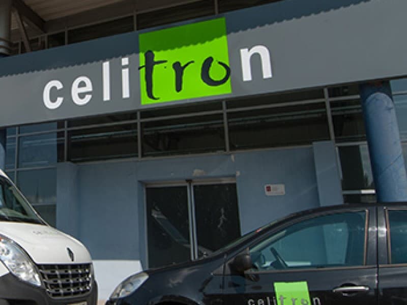 Close-up of the Celitron facility entrance with company-branded vehicles parked in front.