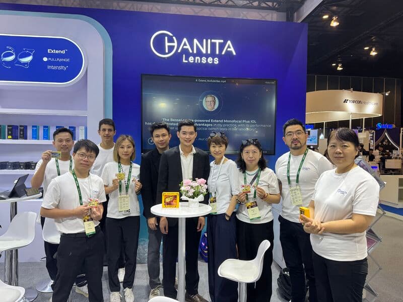 Team members standing at a trade show booth displaying optical lens products and marketing materials.