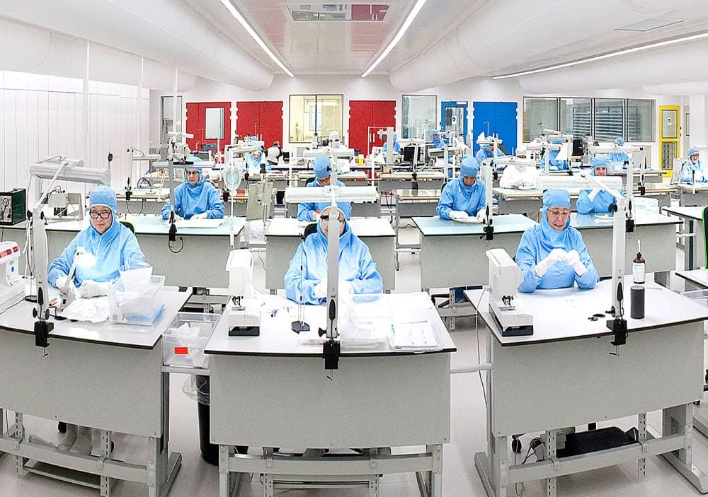 Clean room manufacturing facility with staff in protective gear operating production machinery for medical textile solutions.