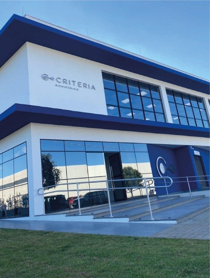 Exterior view of the modern Criteria Biomateriais manufacturing facility with glass facade and company signage.