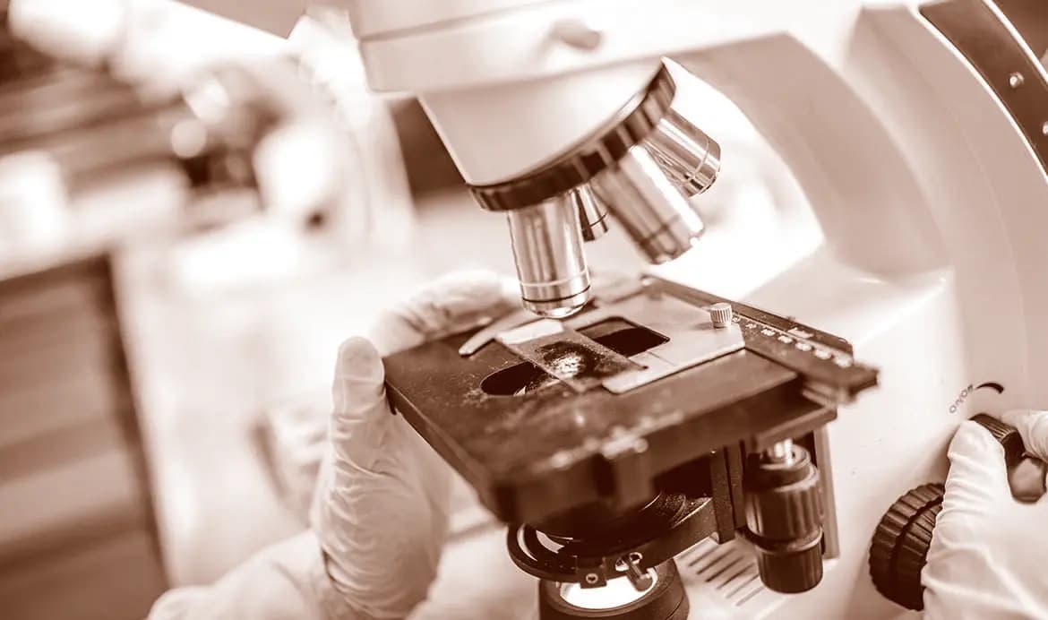 Close-up of a laboratory microscope being used by a technician in a clinical research setting.