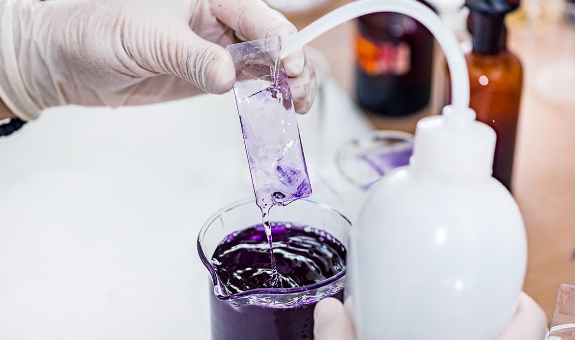 Laboratory technician performing a chemical analysis on a glass slide using a pipette and beaker.