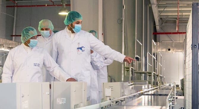 Production team in clean room attire inspecting automated manufacturing equipment on the factory floor.