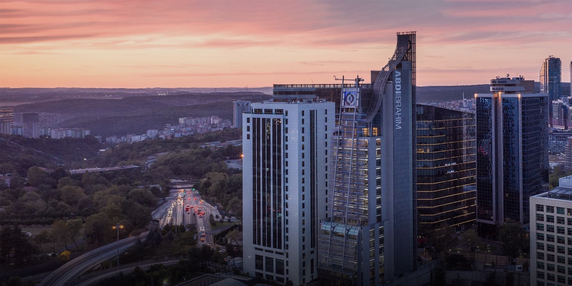 Aerial view of the Abdi İbrahim corporate headquarters building in Istanbul during a sunset, featuring modern glass architecture and surrounding urban landscape.