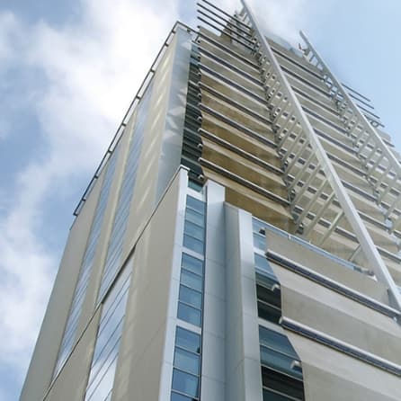 Low-angle view of a modern glass and steel corporate office building exterior against a bright blue sky with light clouds.