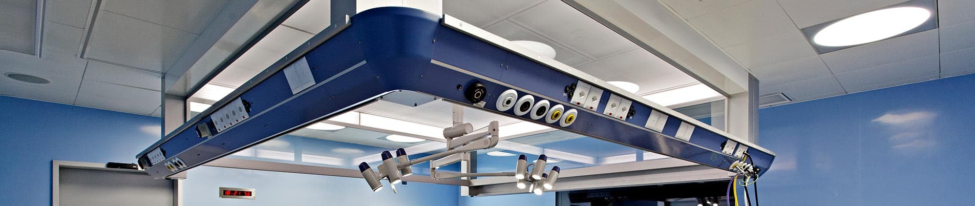 A ceiling-mounted blue medical supply bridge with integrated gas outlets and electrical sockets installed in a modern hospital operating room environment.