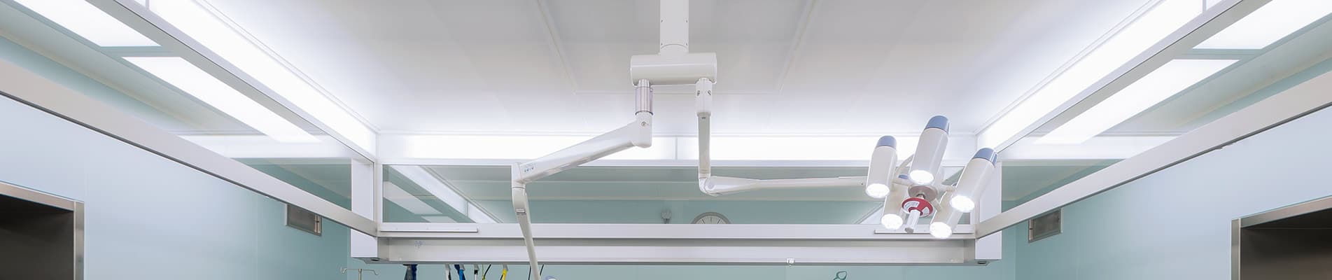 A modern operating room ceiling featuring integrated air ventilation systems and a multi-arm surgical lighting fixture in a sterile clinical environment.