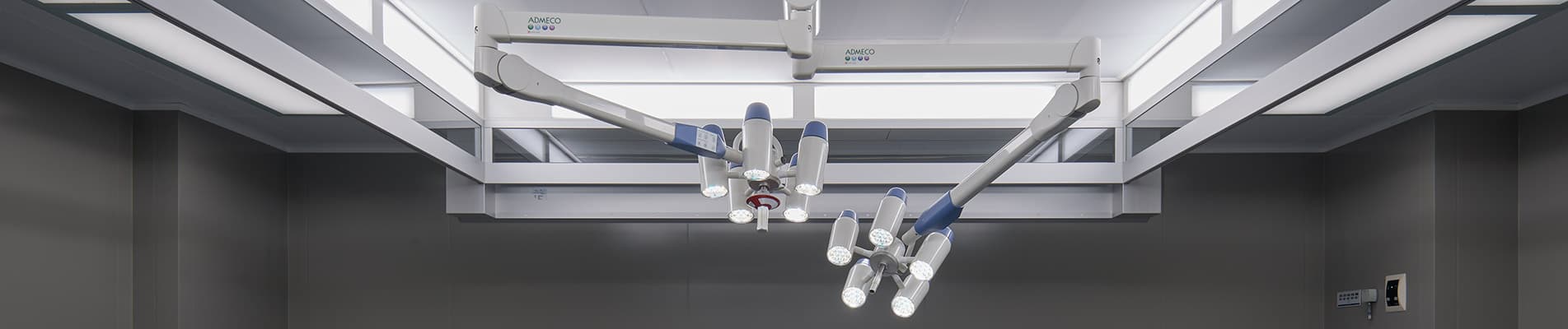 Two ceiling-mounted surgical lighting systems with articulated arms installed in a modern, grey-walled operating room environment.